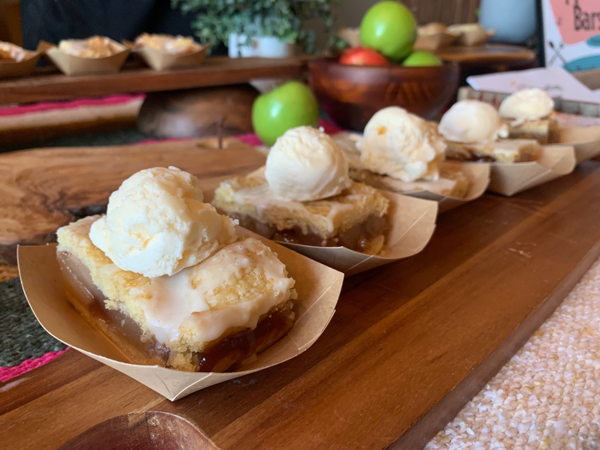 Dessert pastries in paper trays topped with scoops of vanilla ice cream on a wooden table