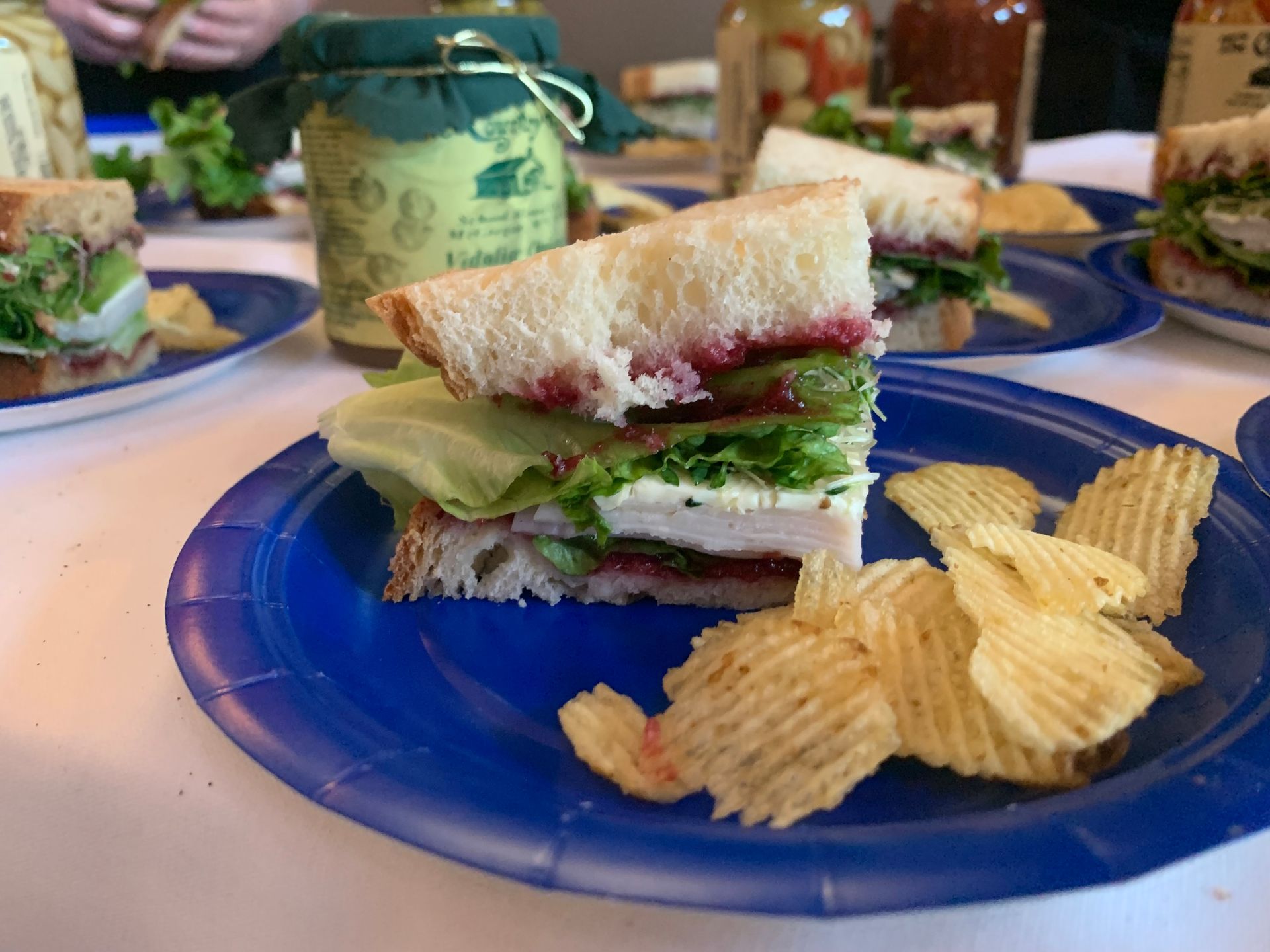 Sandwich halves with lettuce and jam on a blue plate, with ridged potato chips beside them.