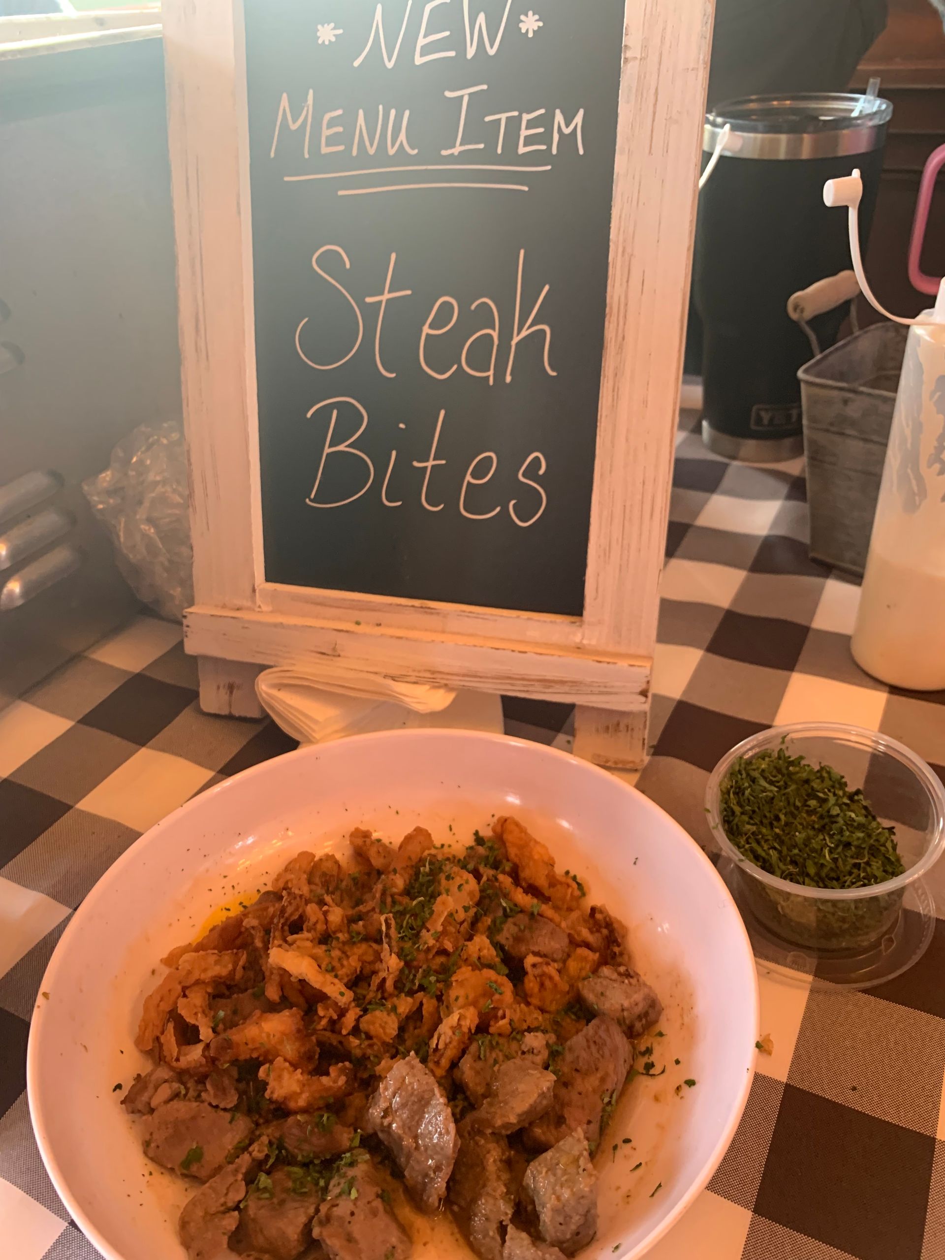 Menu sign for “Steak Bites” beside a bowl of the dish at a restaurant counter