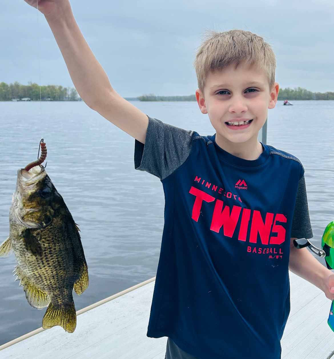 Smiling boy holding up a fish on a boat with a lake in the background