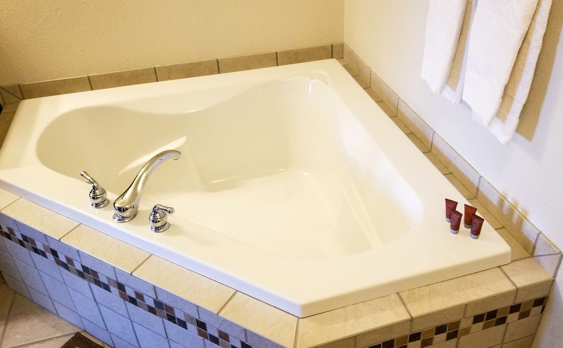 White corner bathtub with chrome faucet and tiled surround in a bathroom.