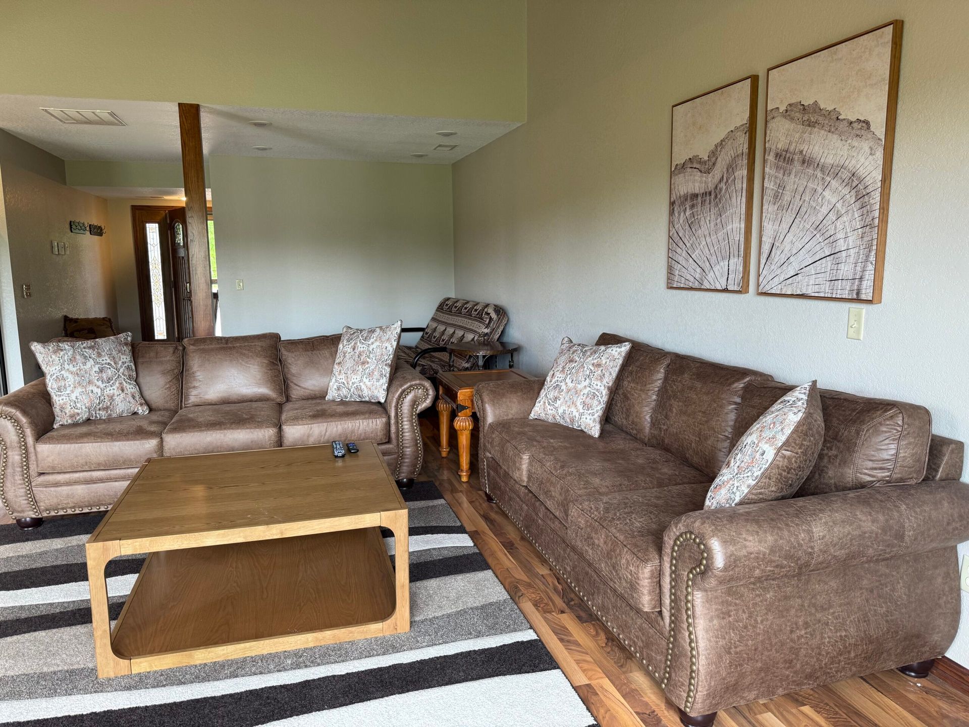 Living room with two brown sofas, striped rug, wooden coffee table, and wall art