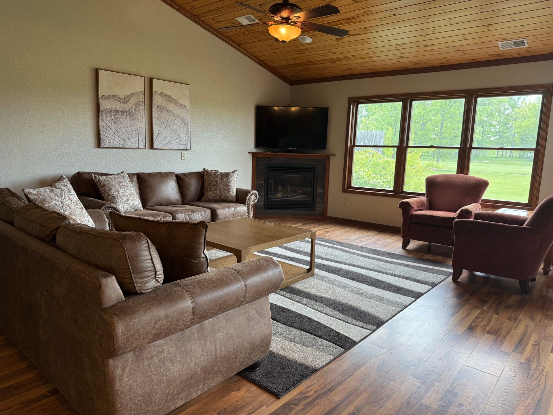 Cozy living room with brown sectional, fireplace, armchairs, striped rug, and large green-window view