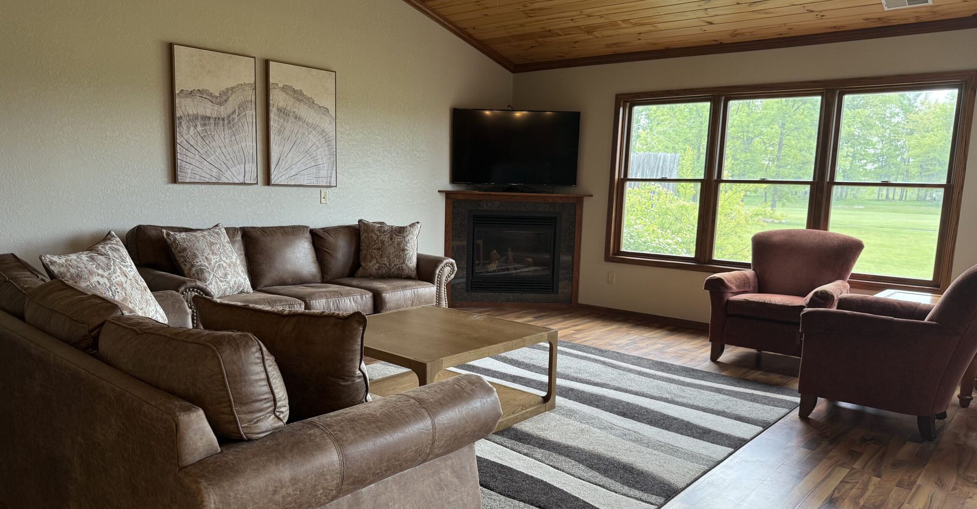 Cozy living room with sectional sofa, fireplace, large windows, striped rug, and two brown armchairs