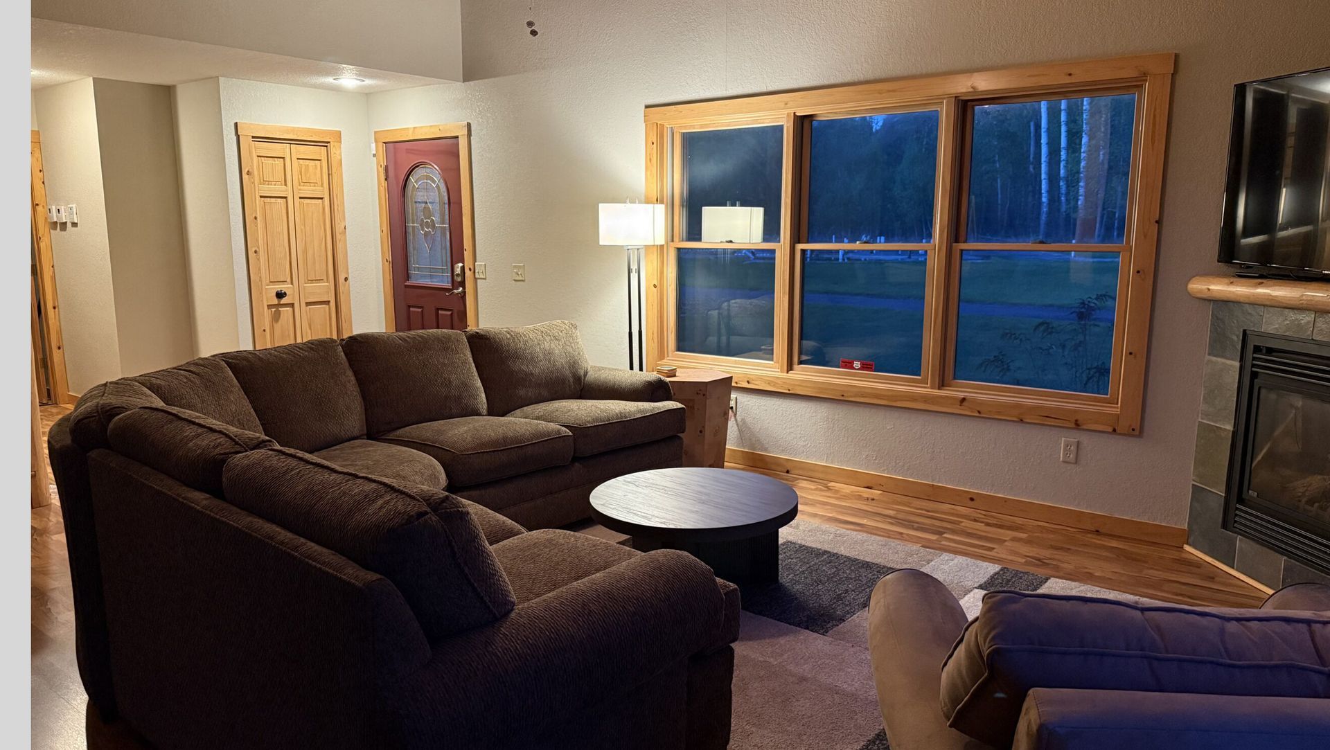 Cozy living room with brown sectional, round coffee table, large windows, and fireplace at dusk