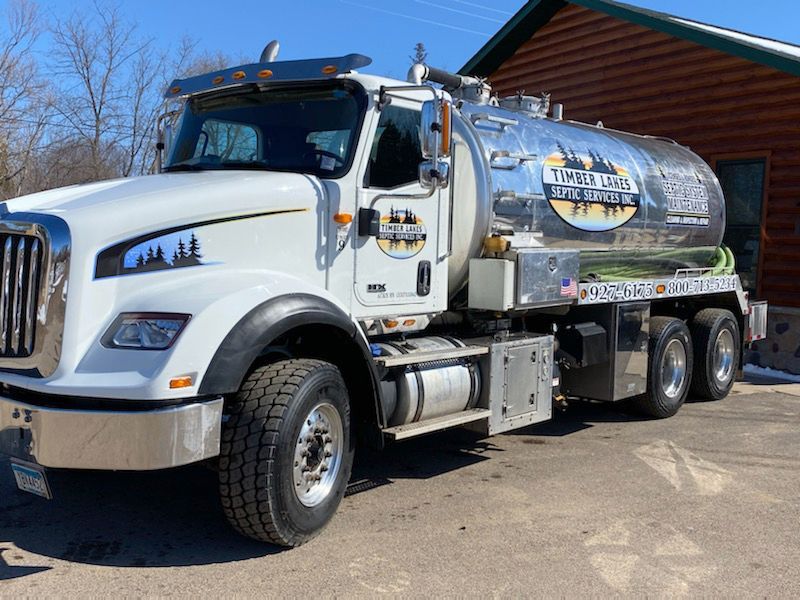 White vacuum truck parked outdoors beside a red building, with a silver tank and blue sky behind it