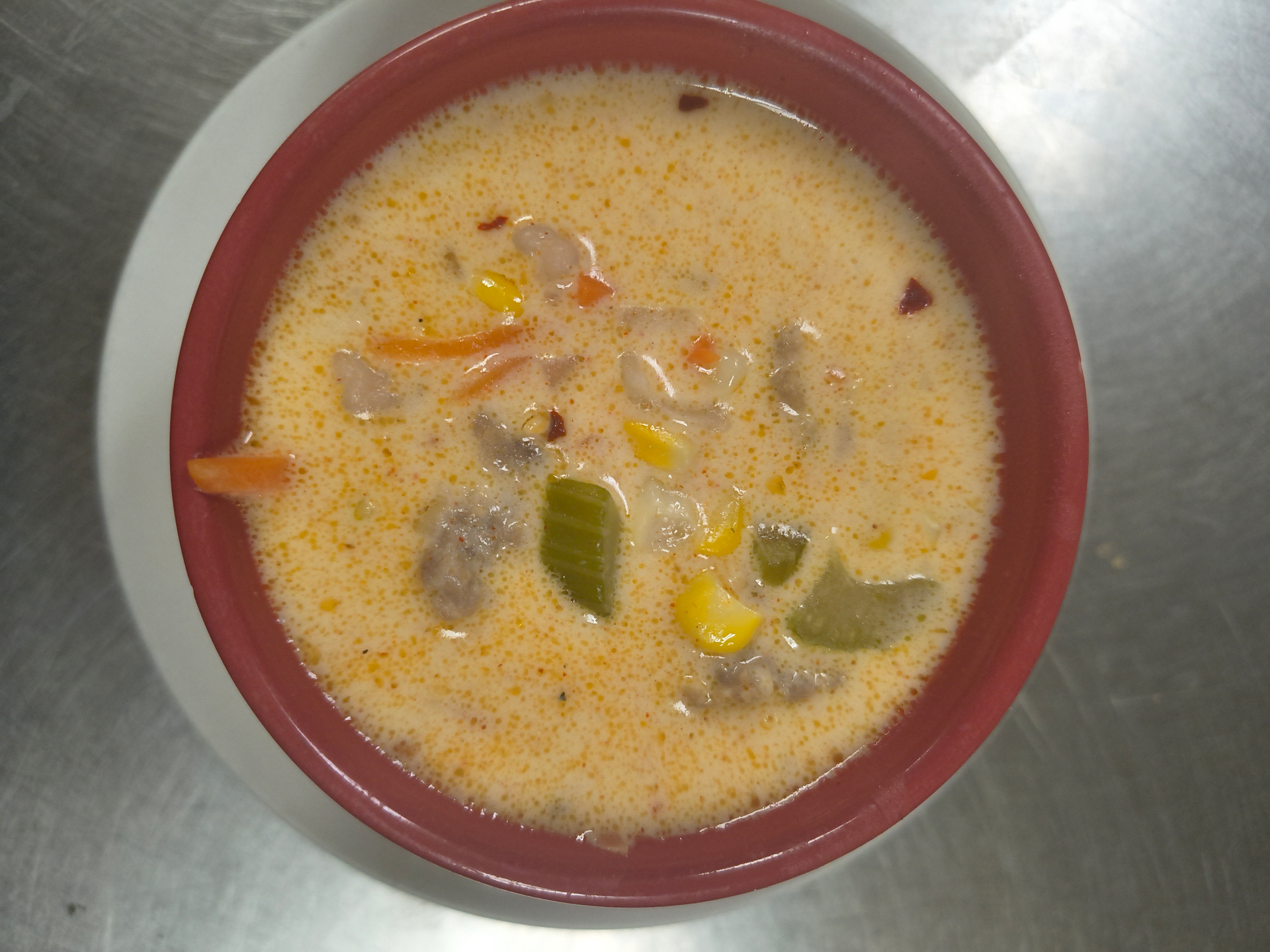 Bowl of creamy soup with vegetables, seen from above on a gray surface