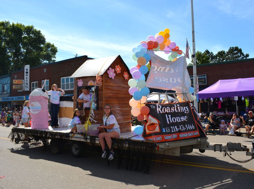 Decorated parade float with balloons and people sitting on a float outside a roast house in sunny weather