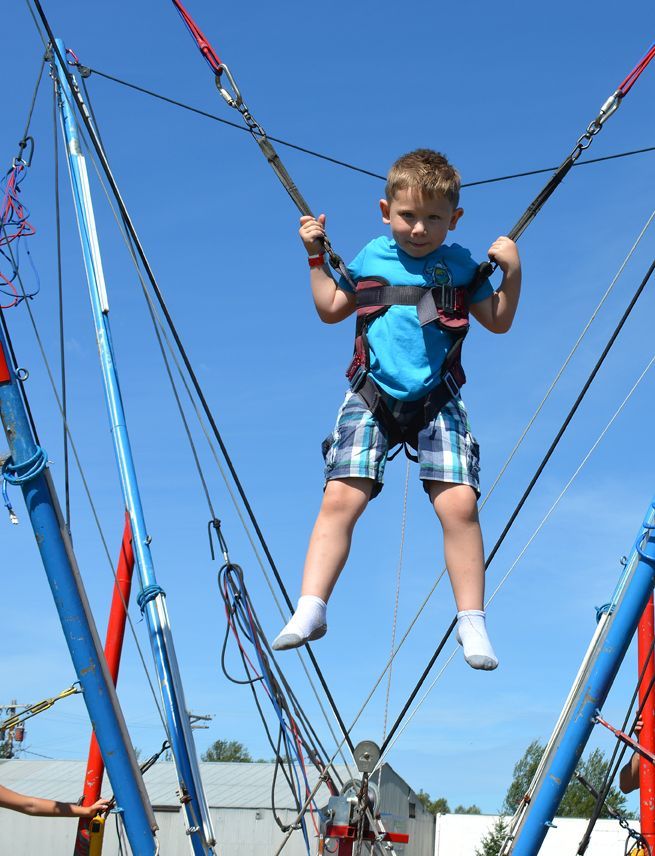 Boy on a bungee trampoline, suspended in harness against a blue sky.