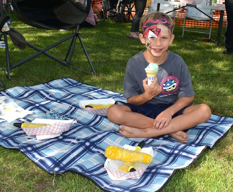 Smiling child sitting on a blue plaid blanket, holding an ice cream cone at a picnic in a park.
