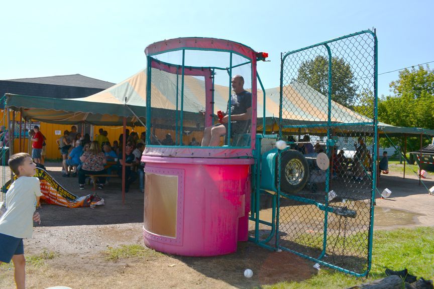 Child on pink bounce house at outdoor fair with tents and tractors in the background