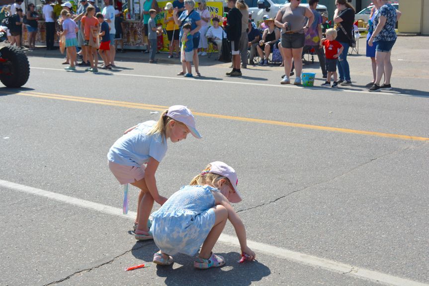 Two children crouch at a race start line while a crowd watches from the sidewalk.