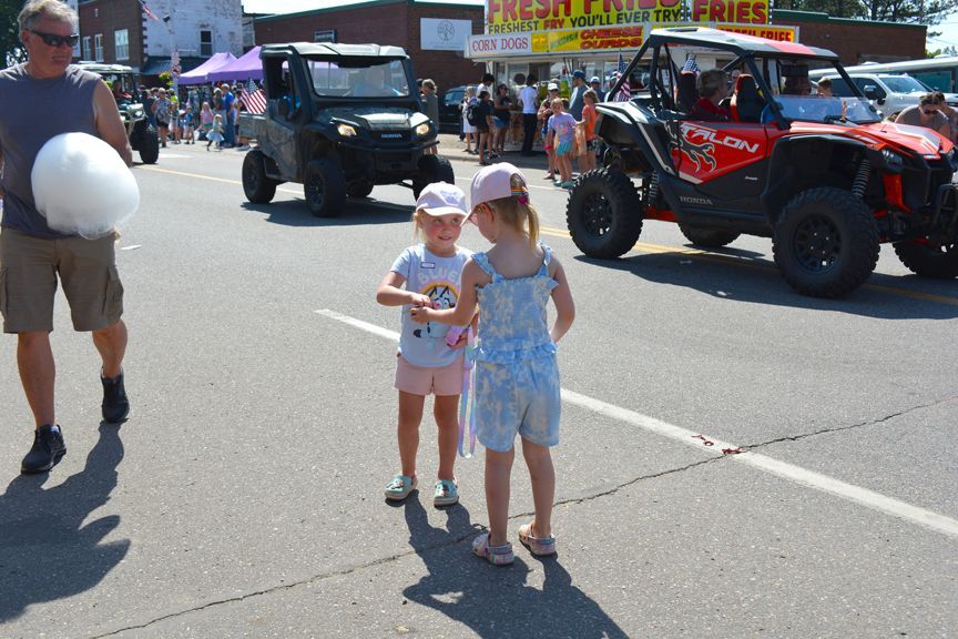 Two children in sun hats standing in a street parade with off-road vehicles in the background