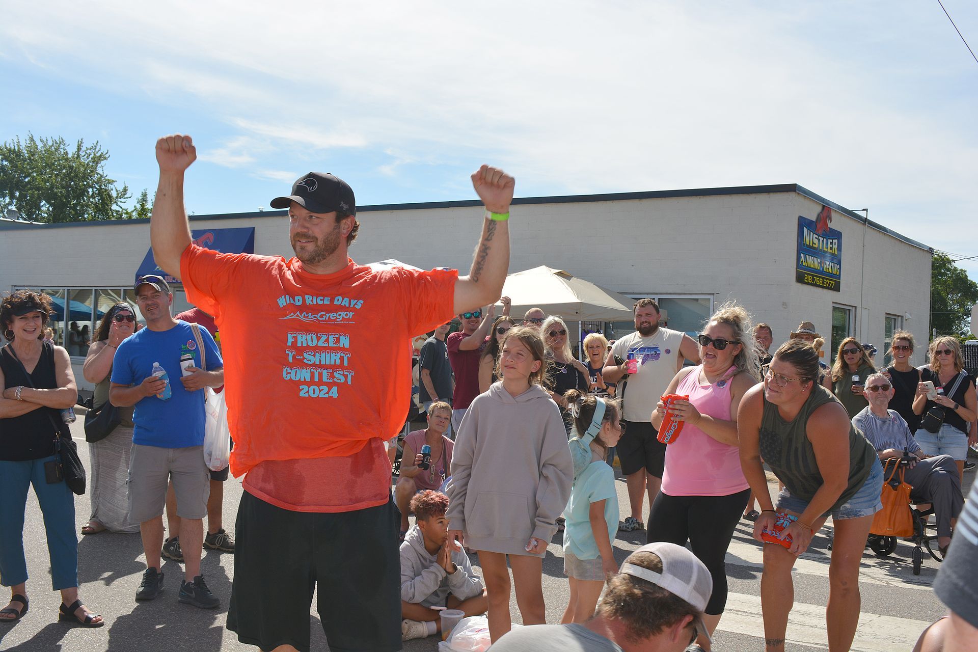 Crowd gathered outdoors as a man in an orange shirt raises both arms in celebration