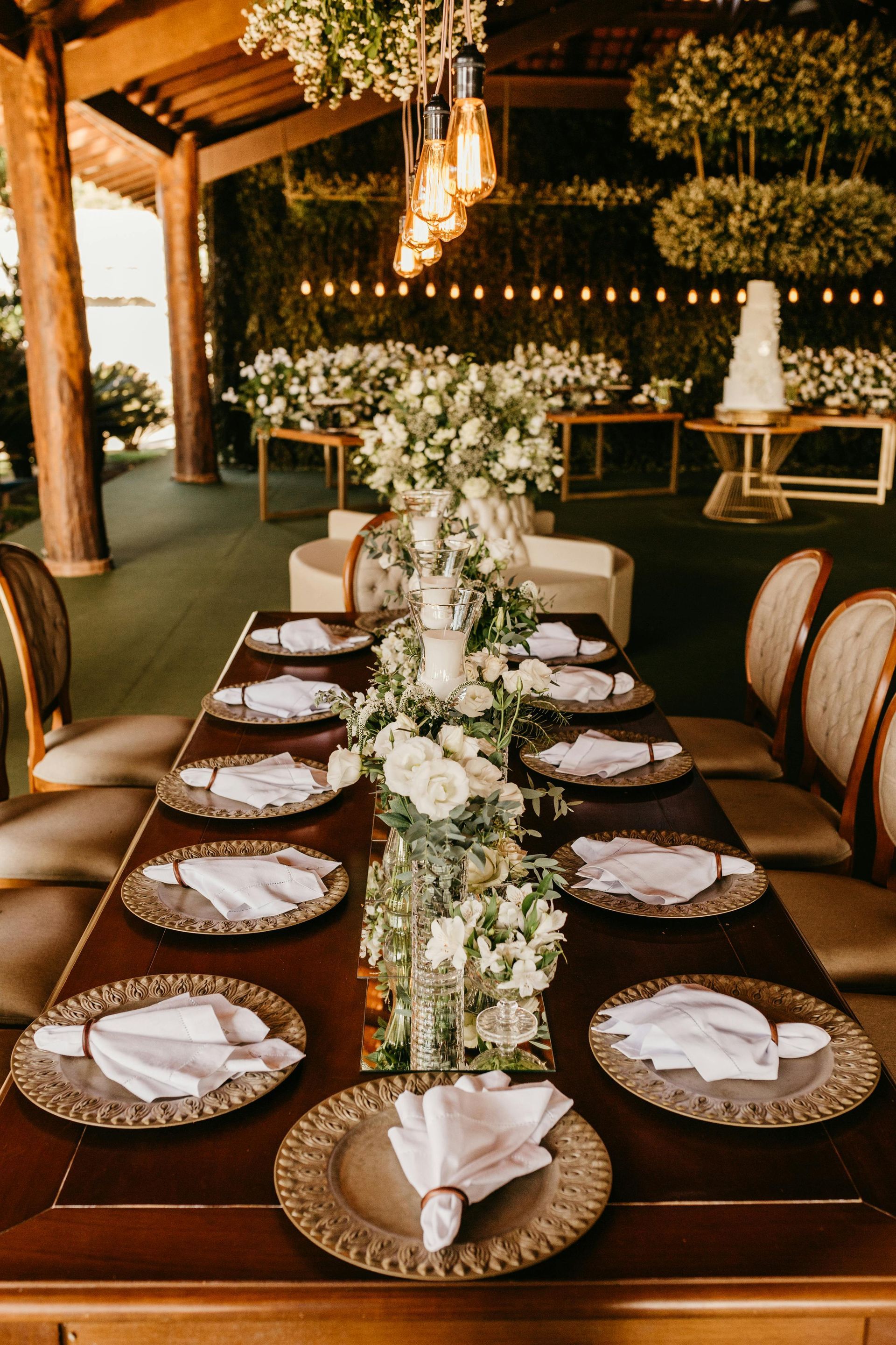 Elegant outdoor dining table set with white floral centerpiece, woven chargers, and candles under a covered patio