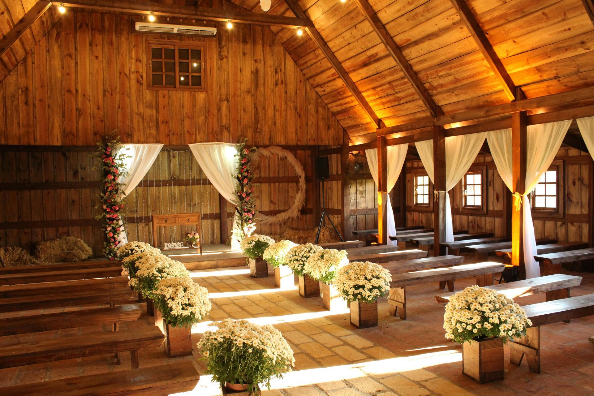 Rustic wooden barn wedding venue with white flowers lining an aisle and sunlight streaming through draped curtains