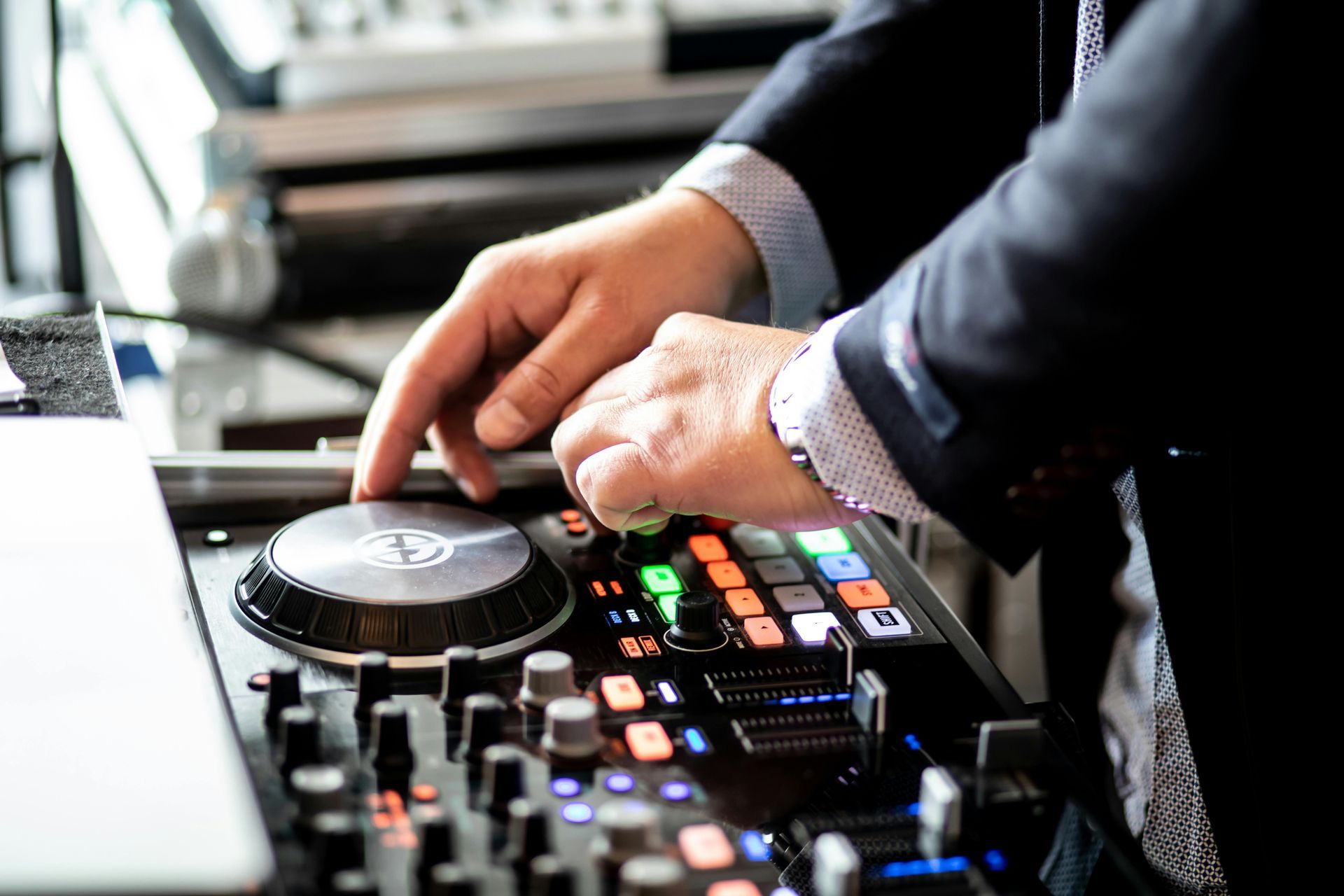 Hands adjusting knobs and buttons on a DJ mixer with colorful illuminated controls