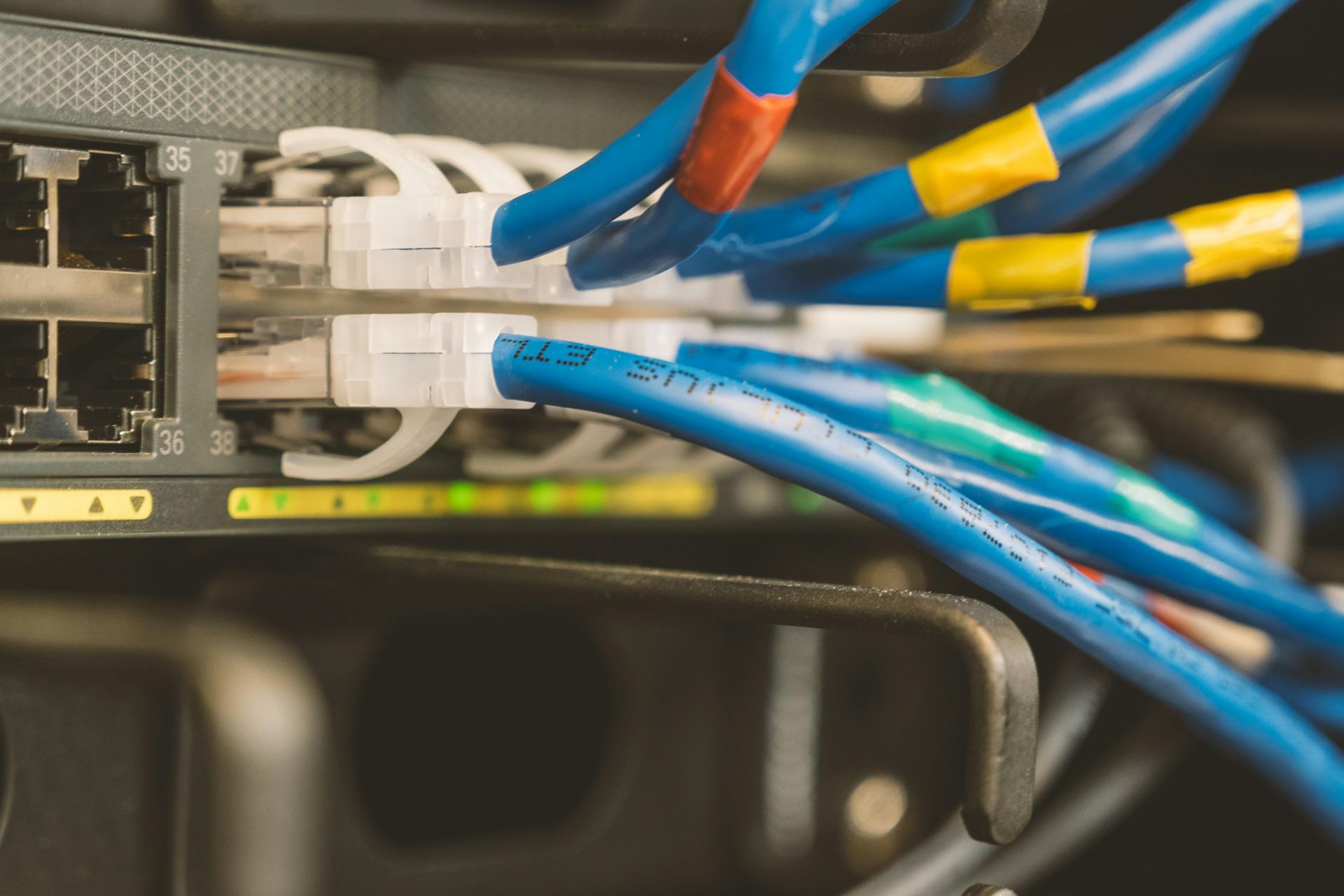 Close-up of network cables plugged into a switch, with blue and yellow wires in a server rack.