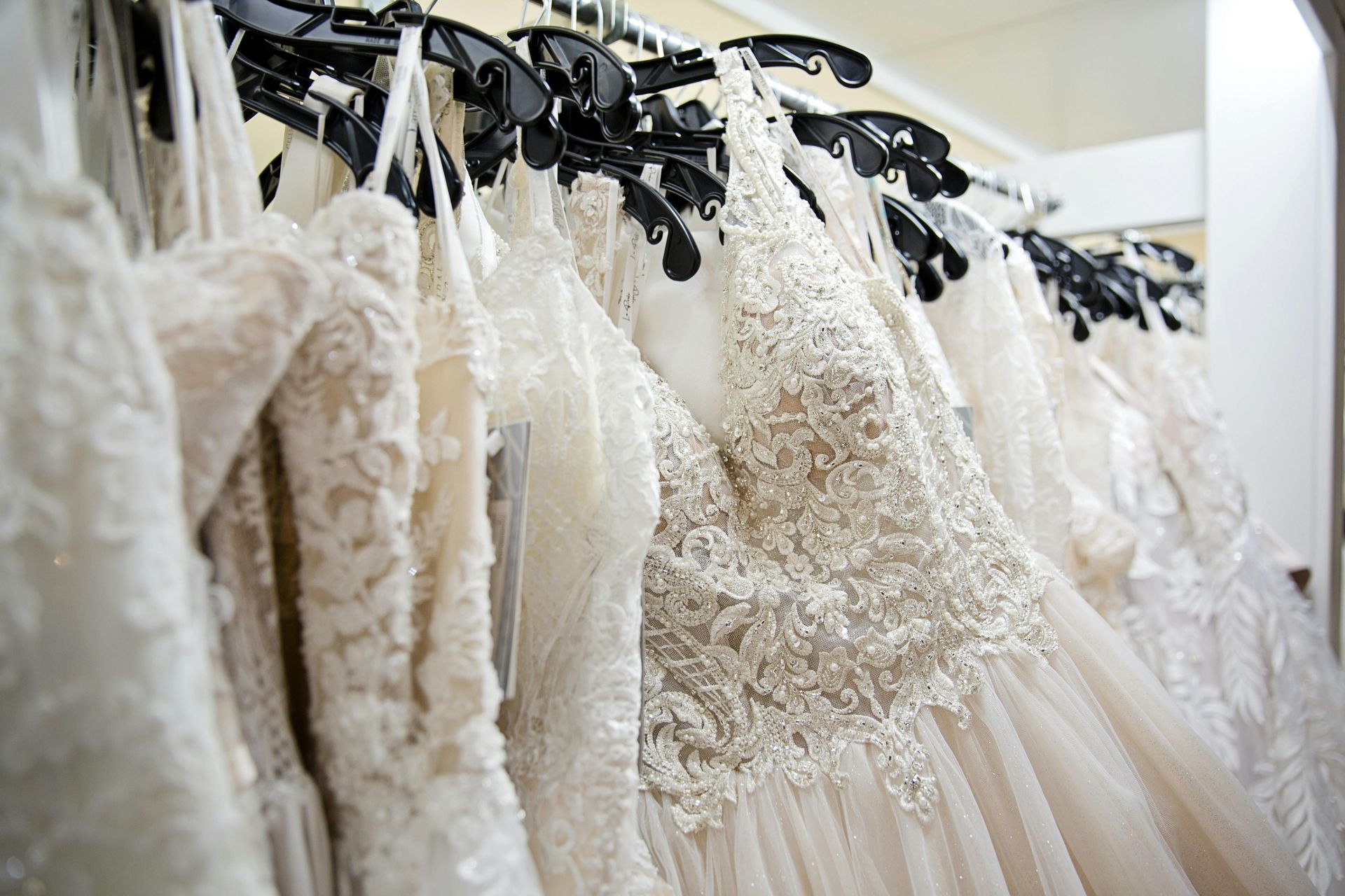 Row of white lace wedding dresses hanging on black hangers in a boutique