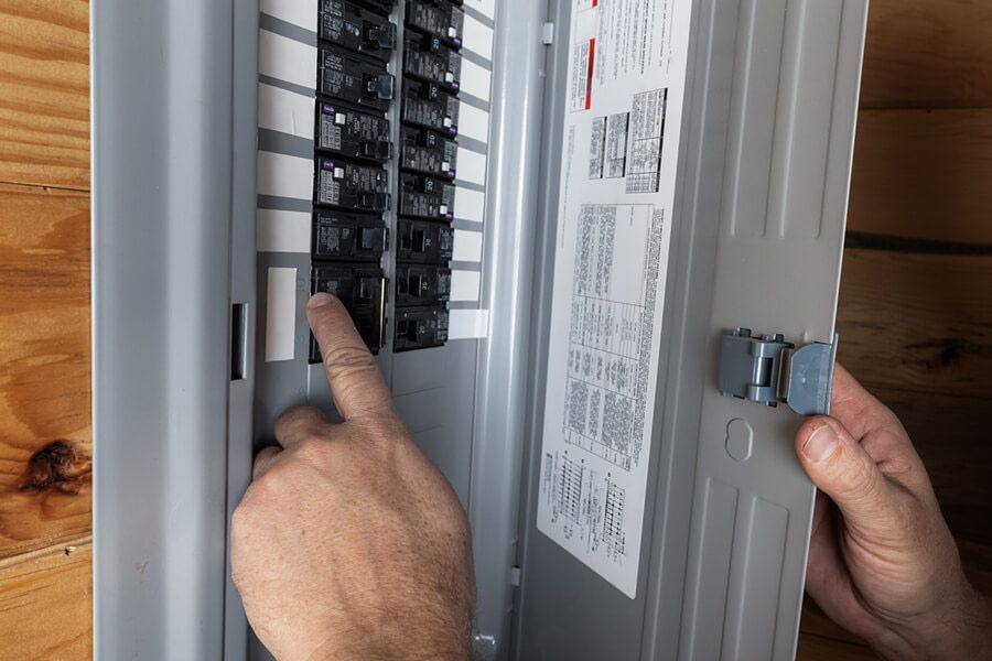 Hands installing a breaker in an open electrical panel indoors.