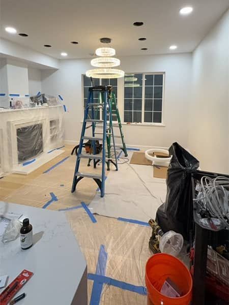 Renovated kitchen with ladders, taped floors, covered cabinets, and exposed ceiling lights during remodeling.