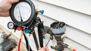 Air conditioning gauges connected to outdoor unit with hoses and valves attached to the refrigerant lines
