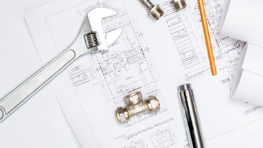 Wrenches, pipe fittings, pencil, and technical plumbing blueprints on a white desk