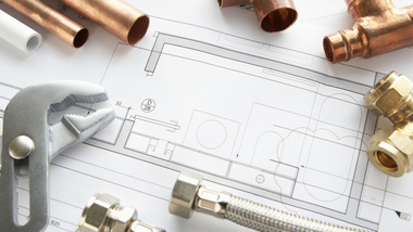 Plumbing tools and copper pipes arranged around a technical blueprint on a worktable