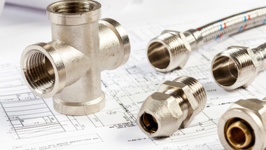 Metal plumbing fittings and flexible hoses arranged on a technical blueprint drawing.