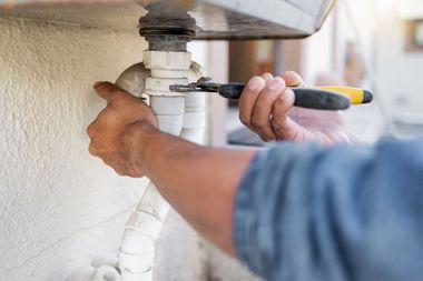 Person using a wrench to tighten a pipe under a sink outdoors