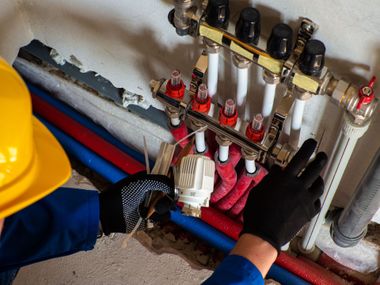 Gloved hands working on colored pipes and valves in a mechanical utility room
