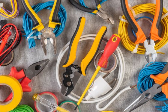 Top-down view of various electrical tools, including pliers, wire cutters, a screwdriver, and coiled wires on a grey surface.