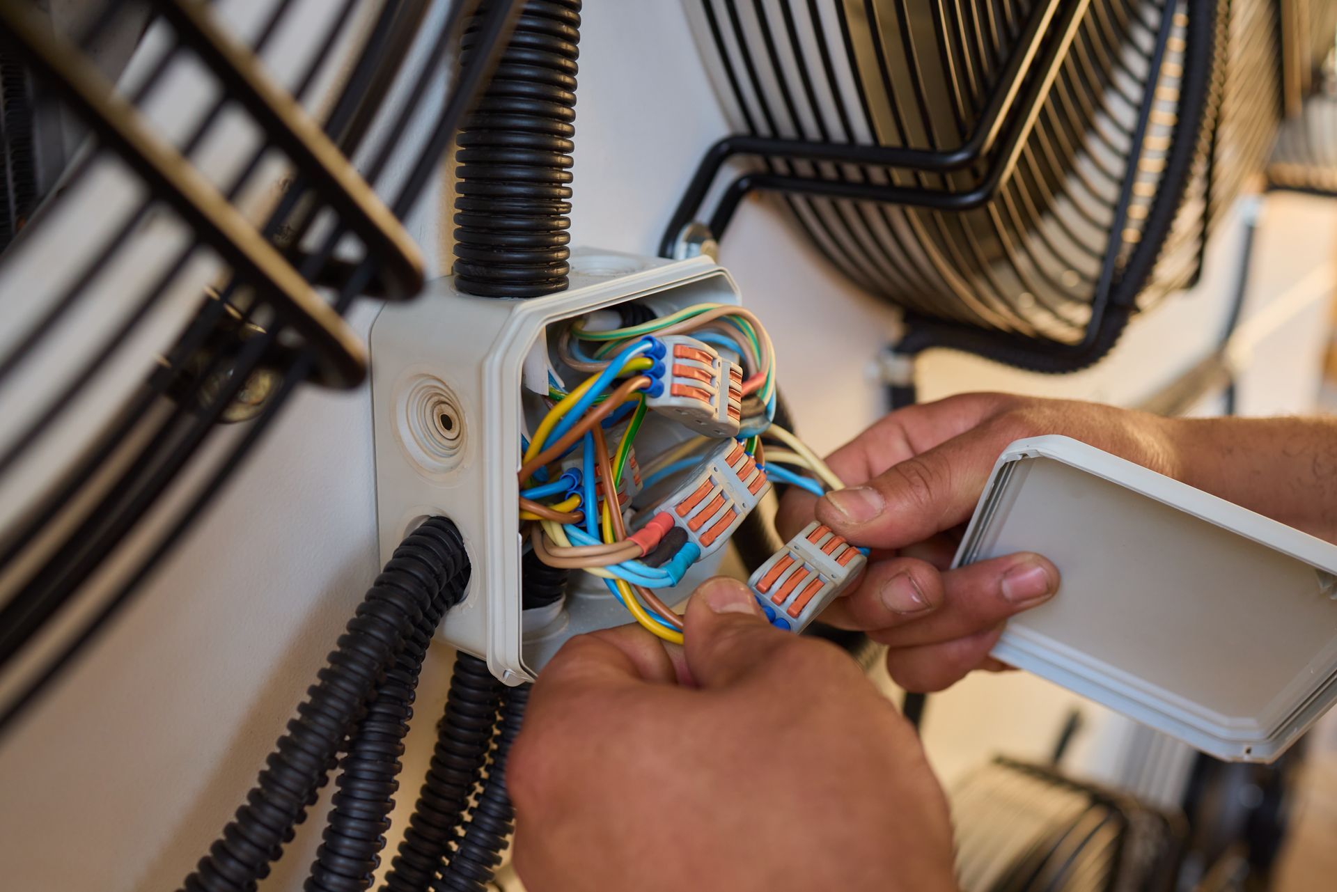 Hands connecting wires inside an electrical junction box mounted on outdoor equipment.