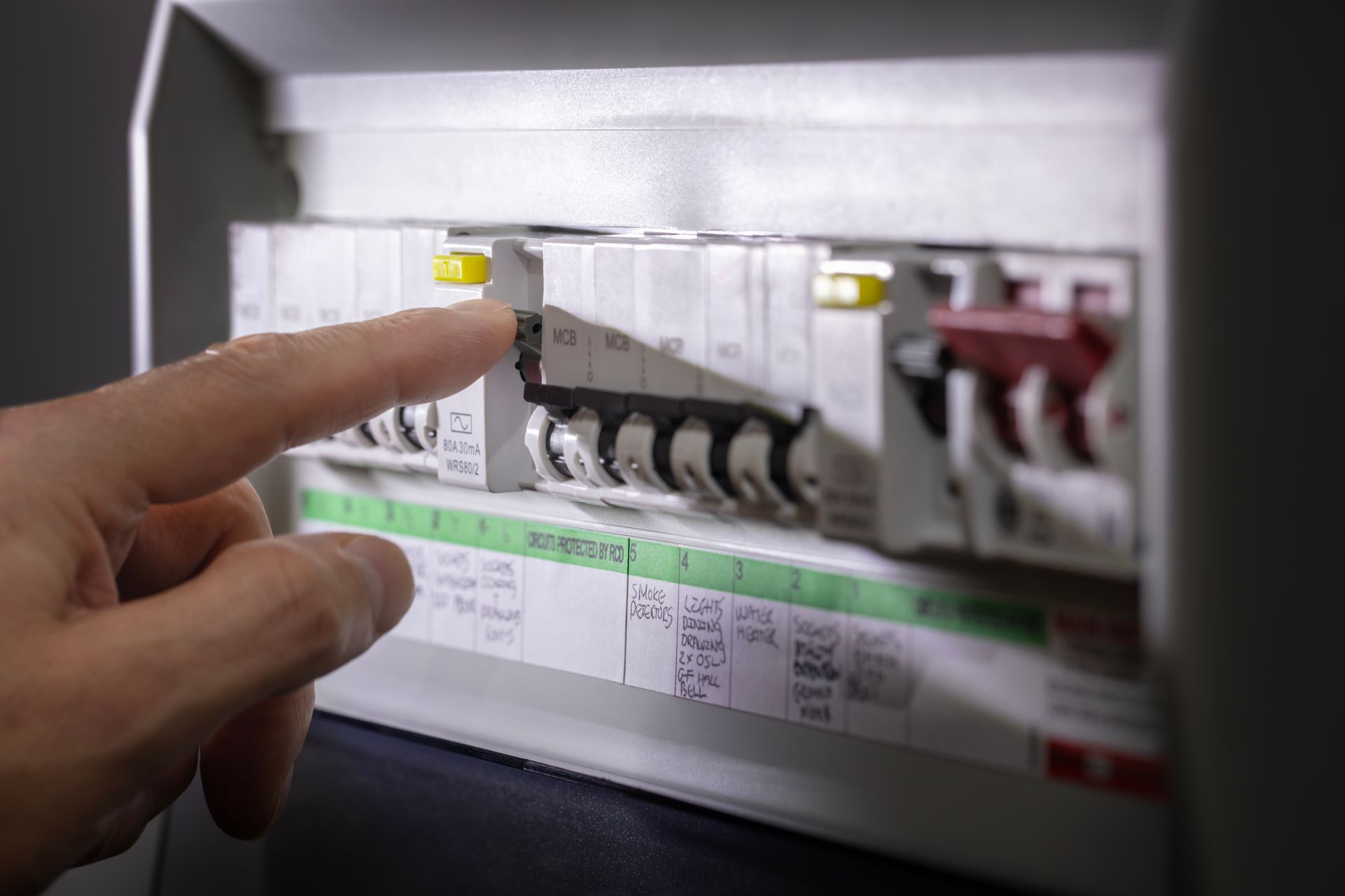 A hand flipping a toggle switch on an electrical circuit breaker panel.
