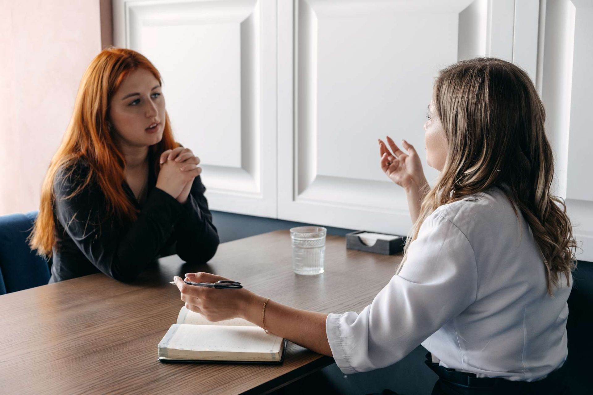 Twee vrouwen zitten aan een tafel en voeren een gesprek.