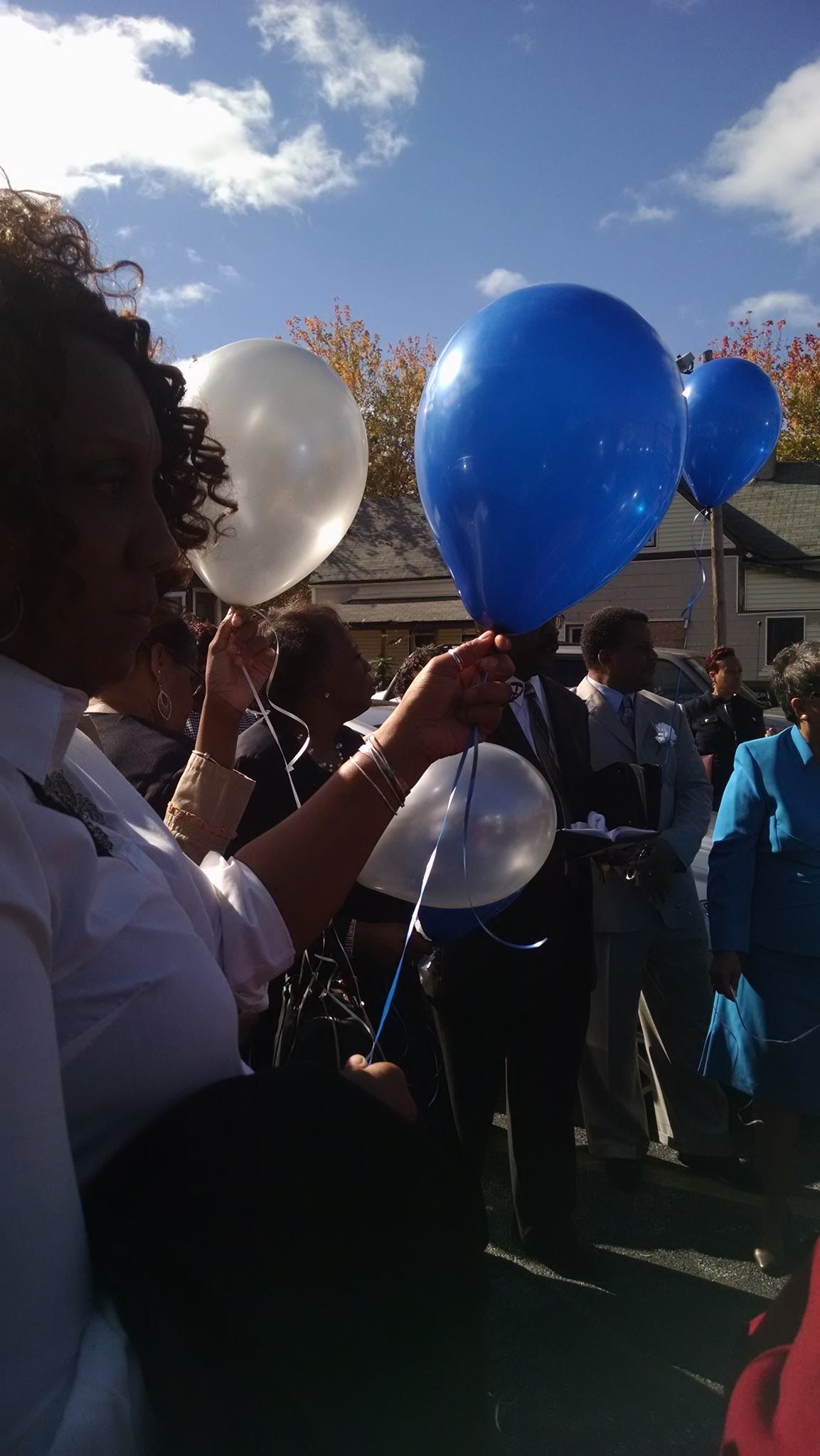 People outdoors holding blue and white balloons at a sunny gathering