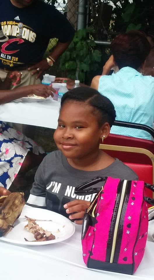 Smiling child seated at a table with a plate of food and a pink backpack beside them