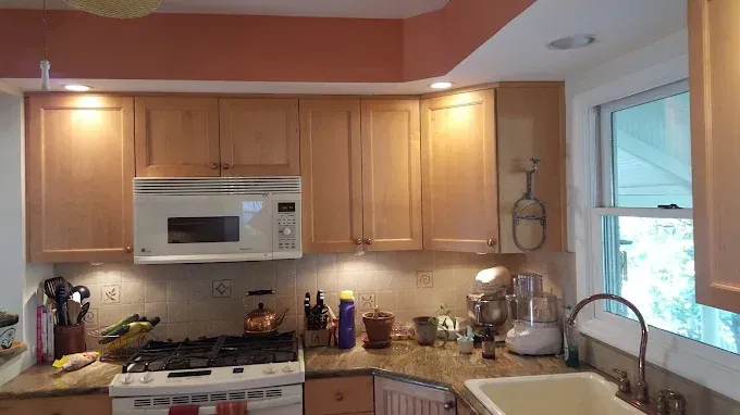A kitchen with wooden cabinets , a stove , a microwave , a sink , and a window.