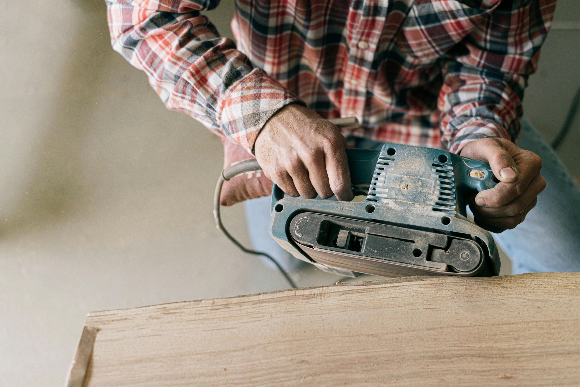 A man is sanding a piece of wood with a belt sander.