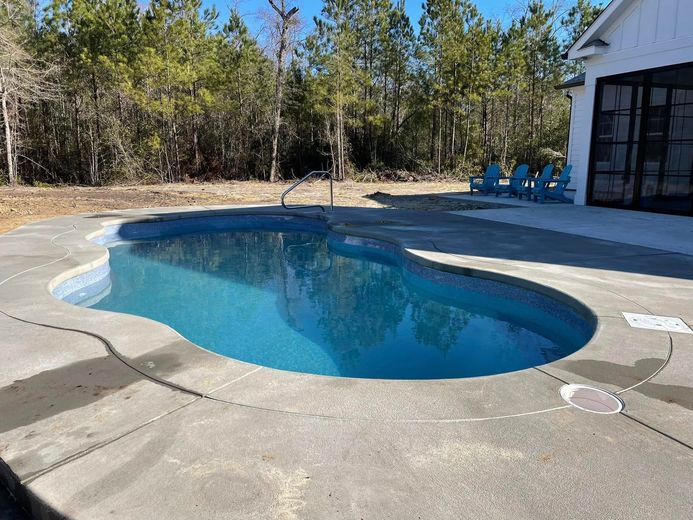 Backyard swimming pool with a curved concrete deck and trees in the background