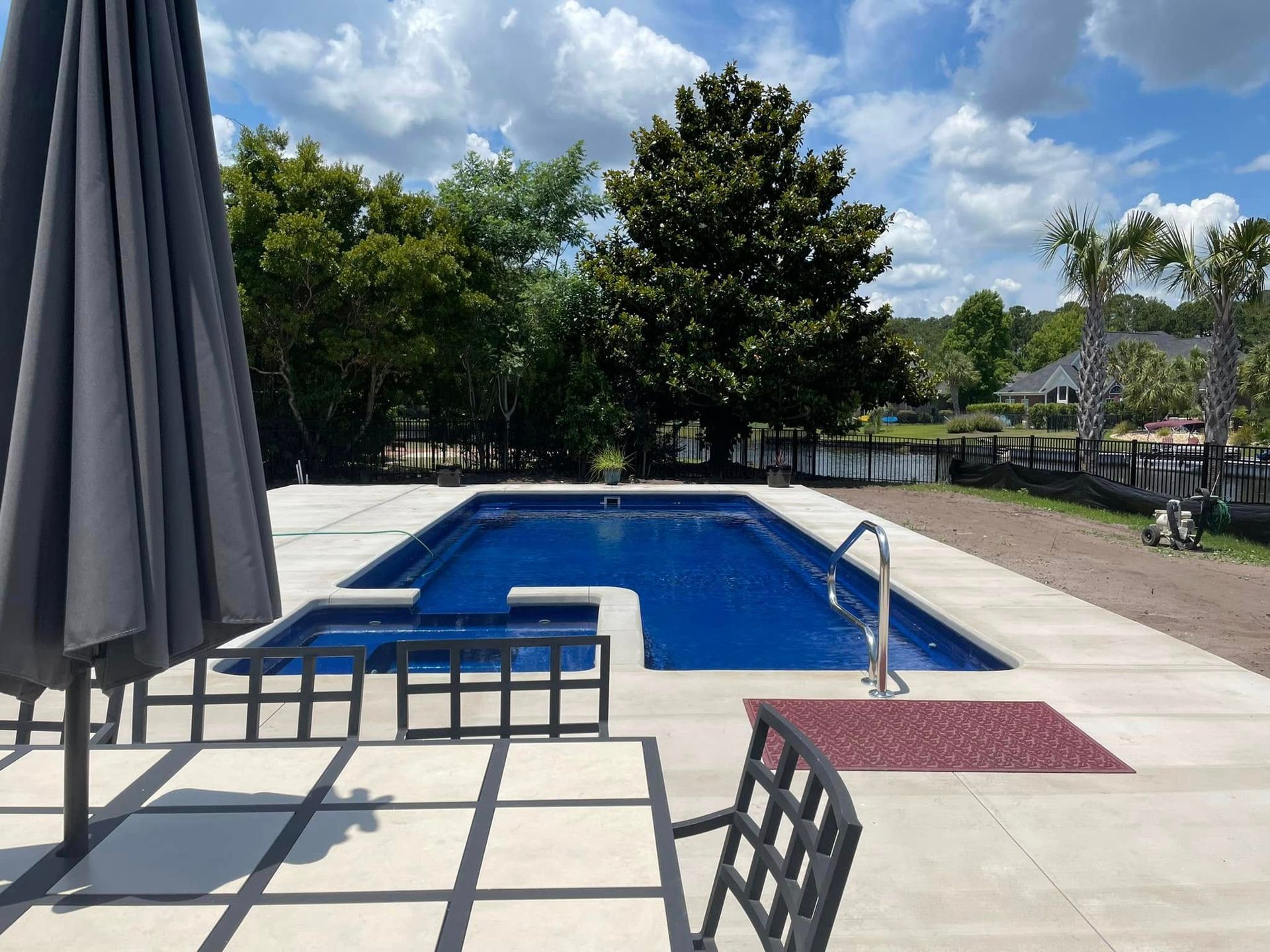 Outdoor pool with blue water, lounge chairs, and a shaded patio under a partly cloudy sky