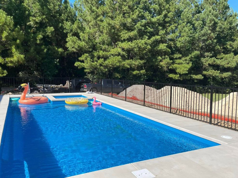 Backyard swimming pool with floaties and a fenced, tree-lined patio
