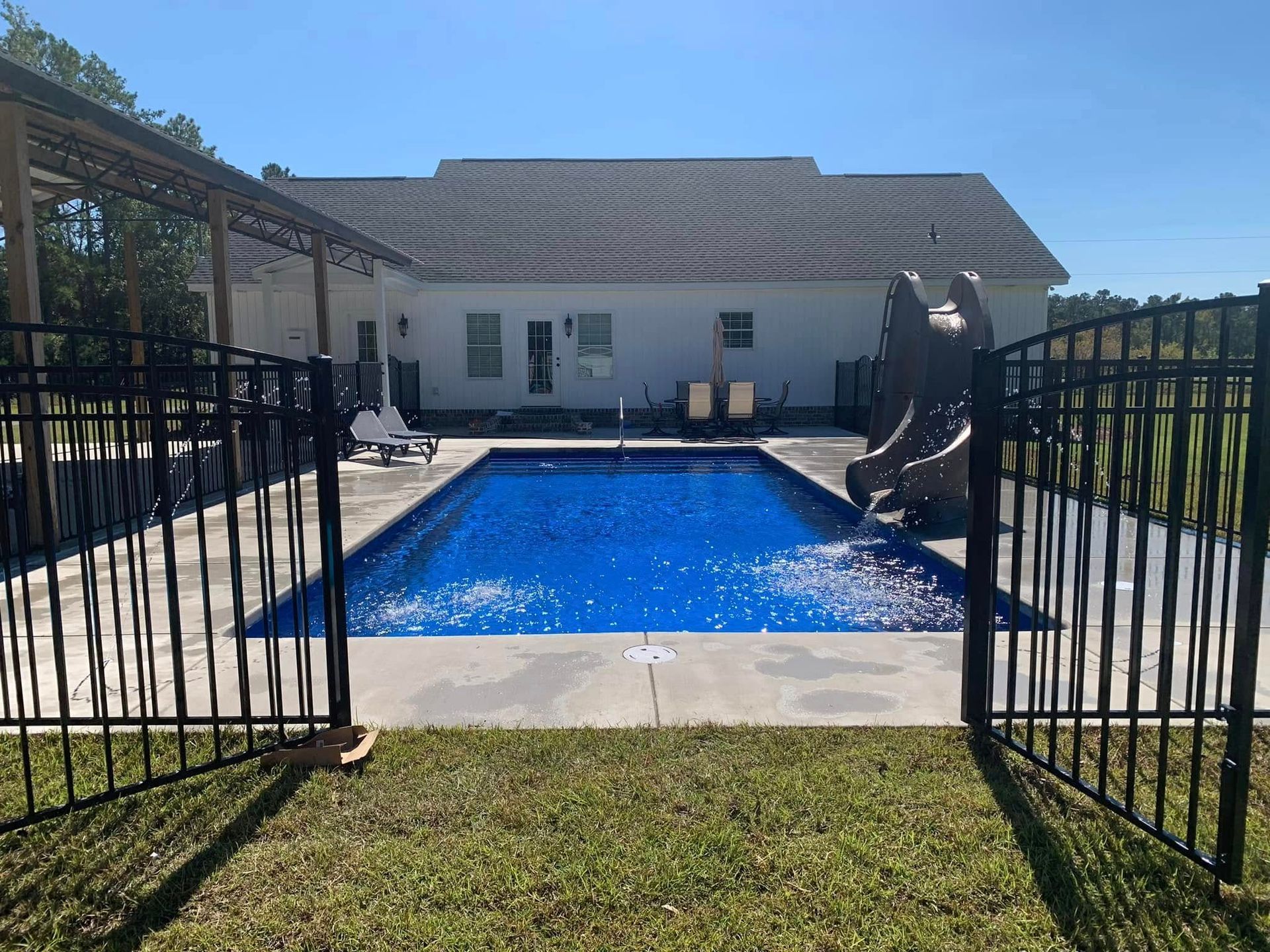 Backyard pool with blue water behind open black gates and a white house in the background