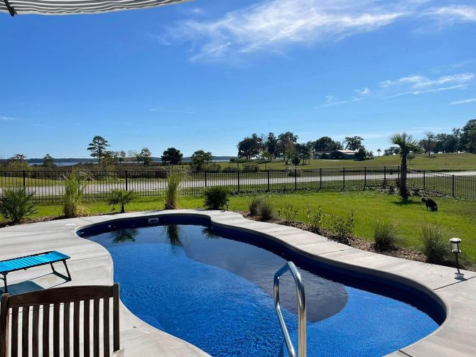 Backyard pool with blue water, patio chairs, and a fenced grassy field under a sunny sky