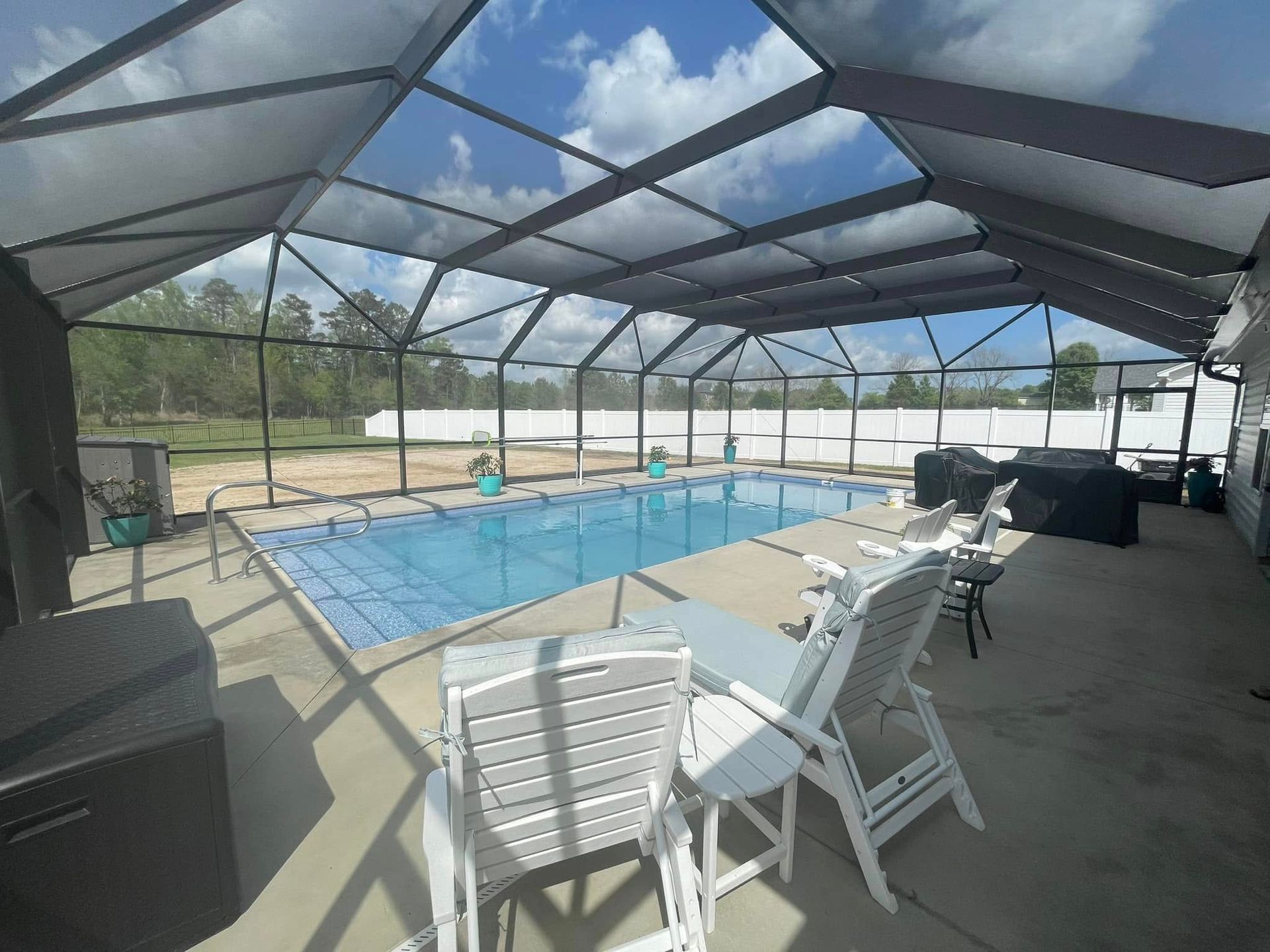 Screened-in pool patio with covered swimming pool and white lounge chairs under a blue sky