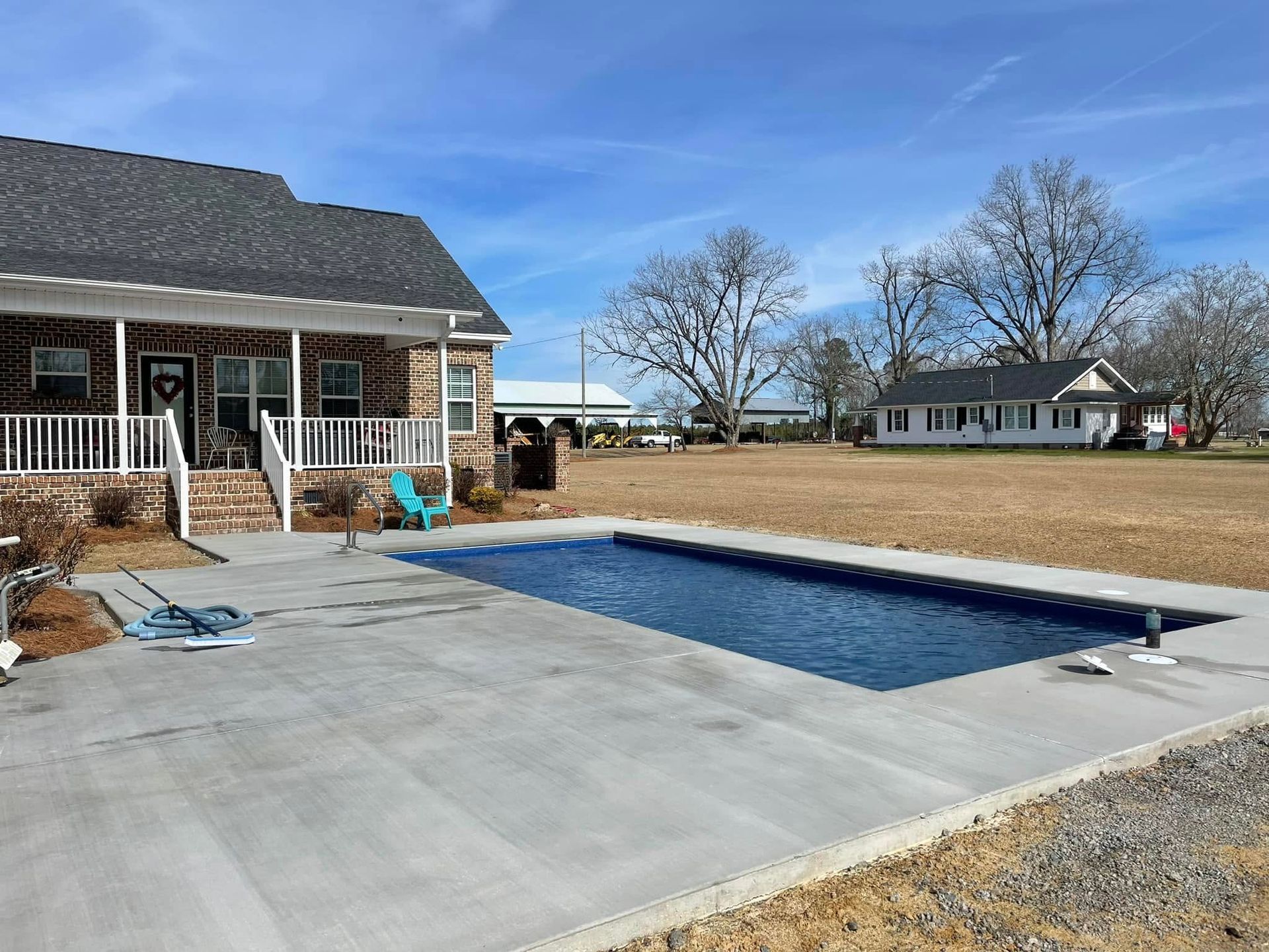Backyard with a rectangular in-ground pool beside a house on a sunny day