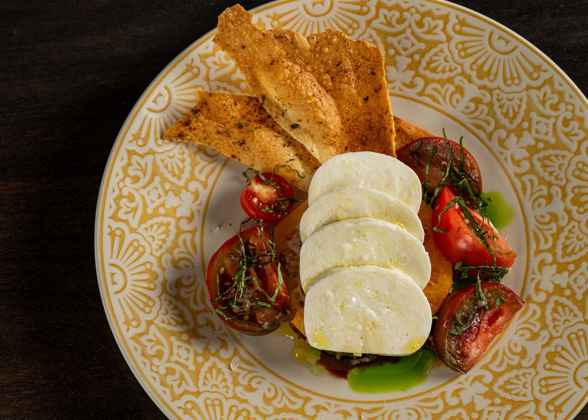 A plate of food with tomatoes , mozzarella and crackers on a table.