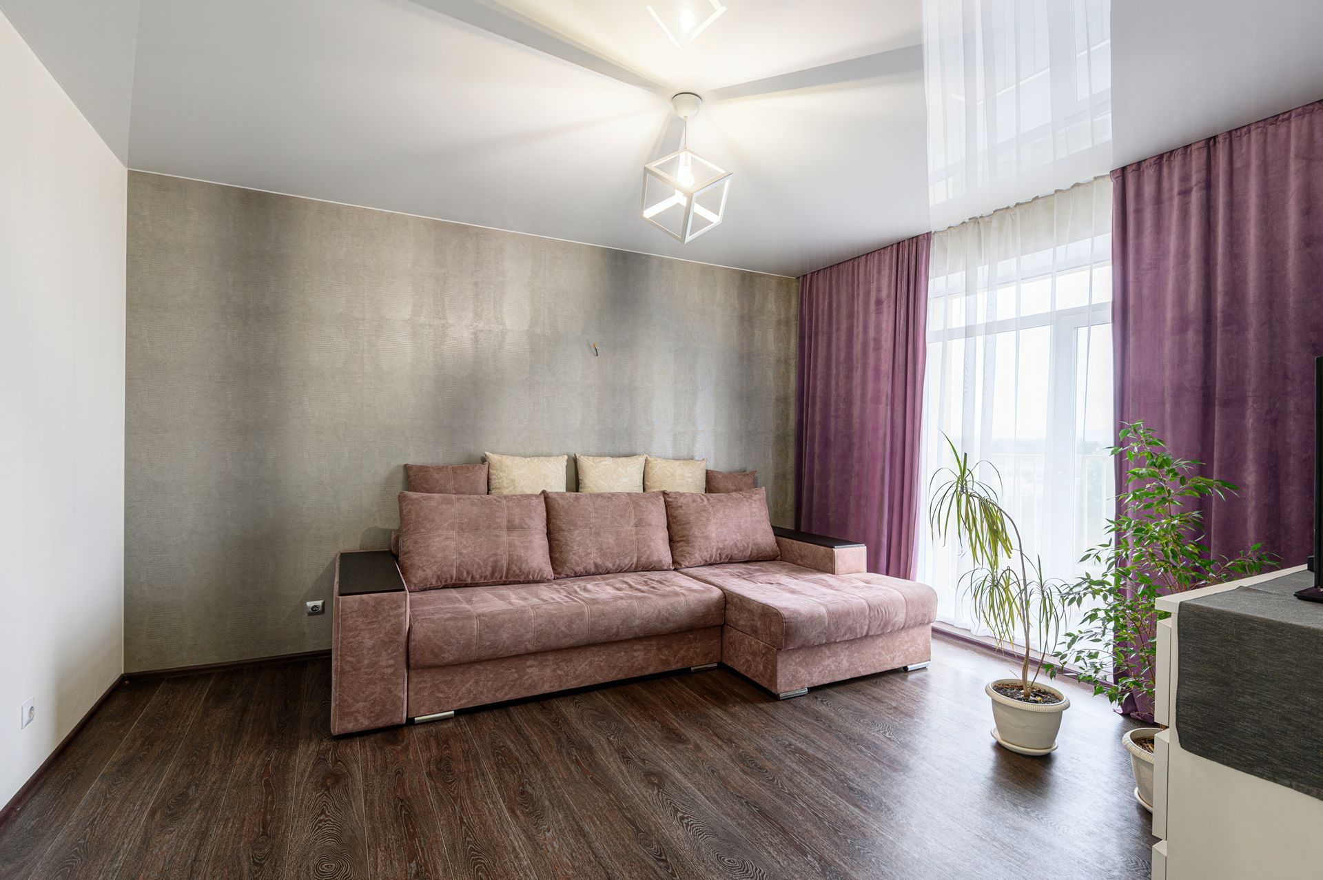 Bright living room with a mauve sofa, dark wood floor, and large window with purple curtains.