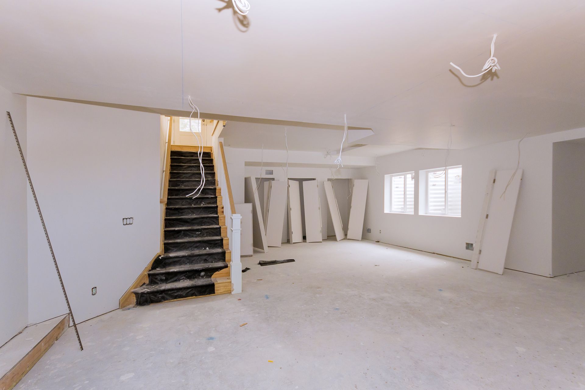 Unfinished room with white walls, exposed stairs, and construction materials on the floor.