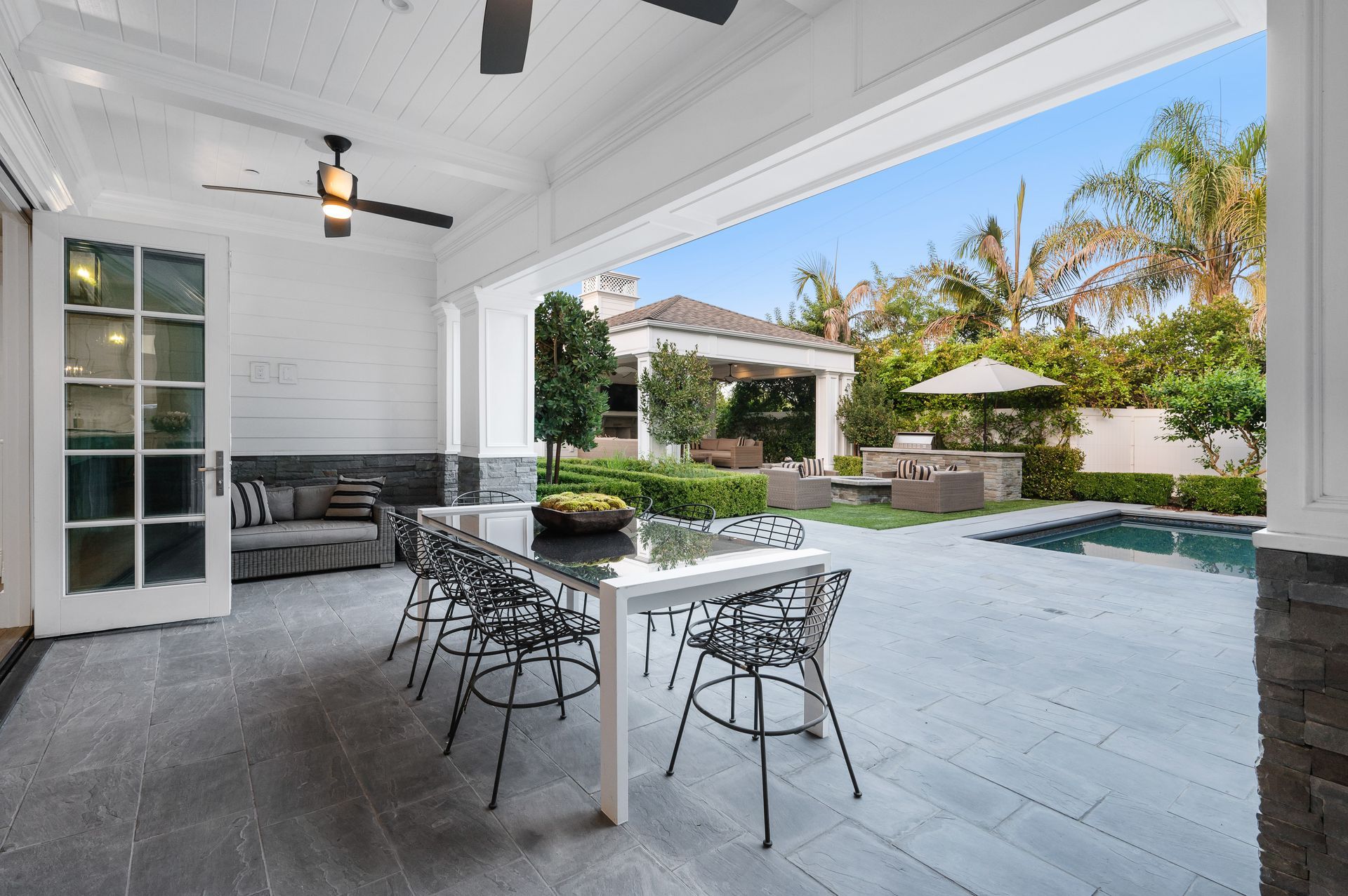 Covered patio with dining table, chairs, and a view of a backyard pool and tropical landscaping Covered patio with dining table, chairs, and a view of a backyard pool and tropical landscaping